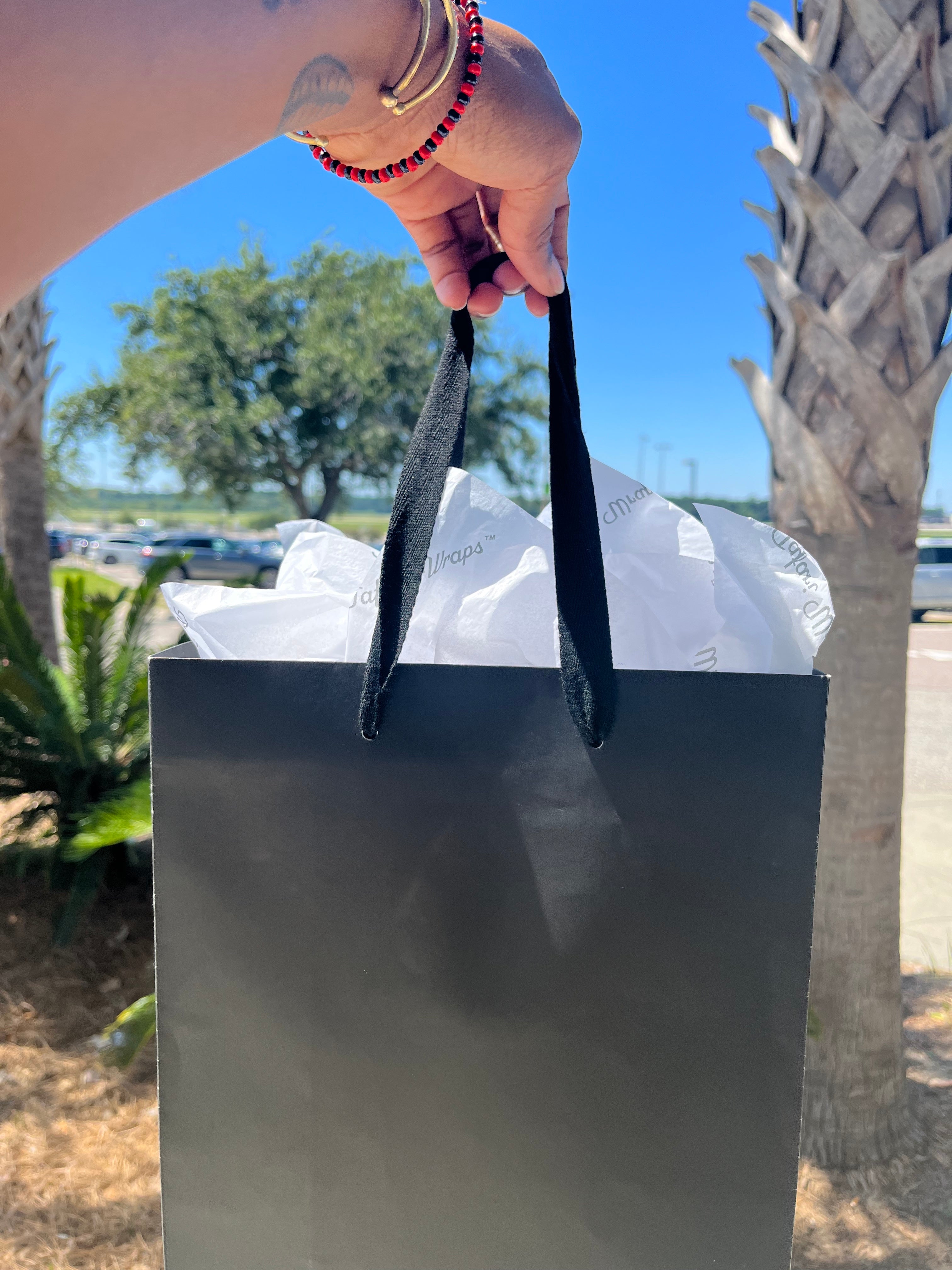 Black shopping bag with Tafari Wraps tissue paper in the sun